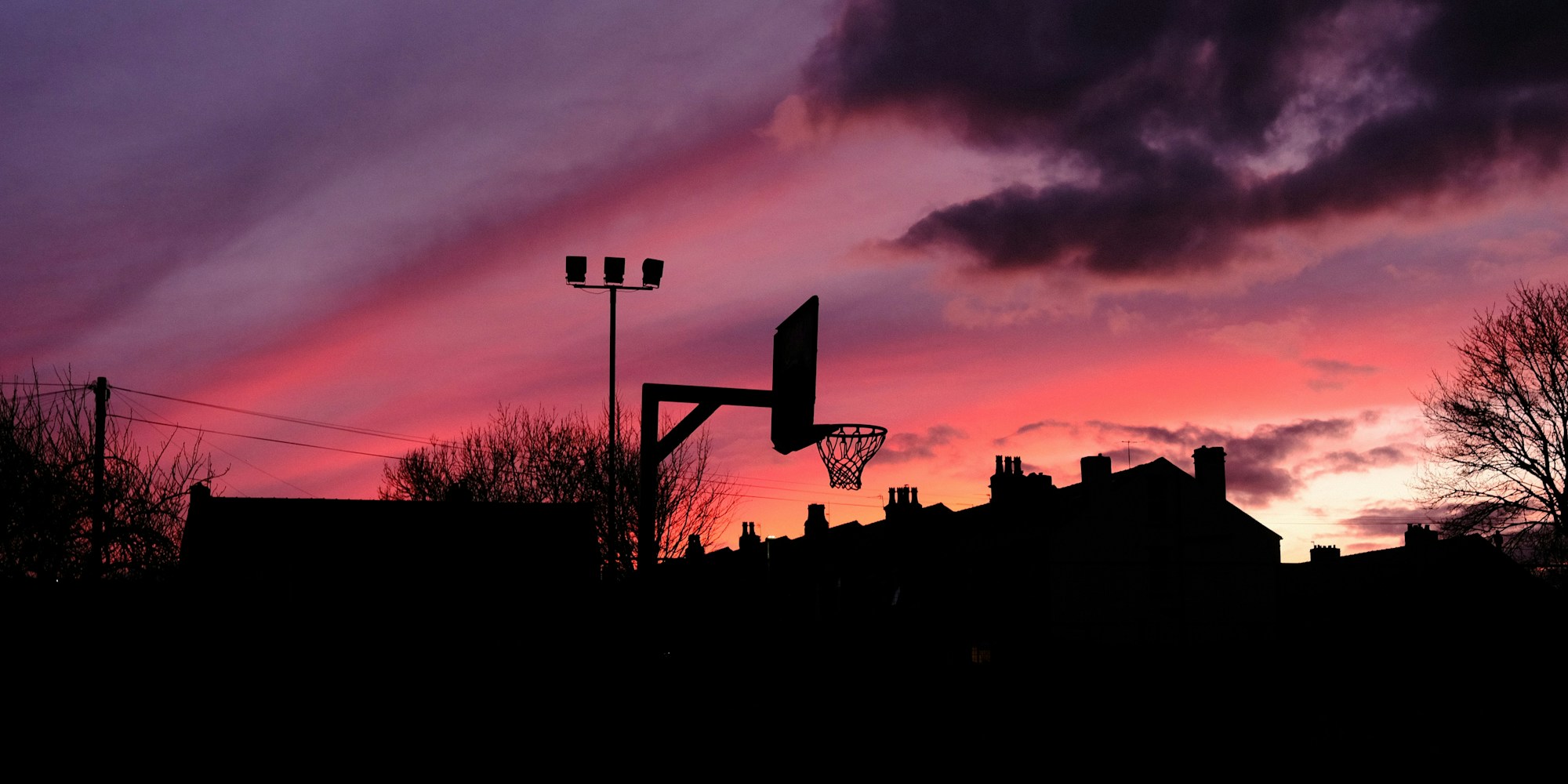 A basketball hoop silhouetted against an orange and purple sunset